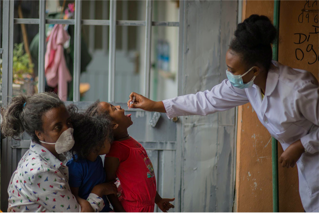Child receiving oral polio vaccine in Ethiopia from a healthcare worker in a mask